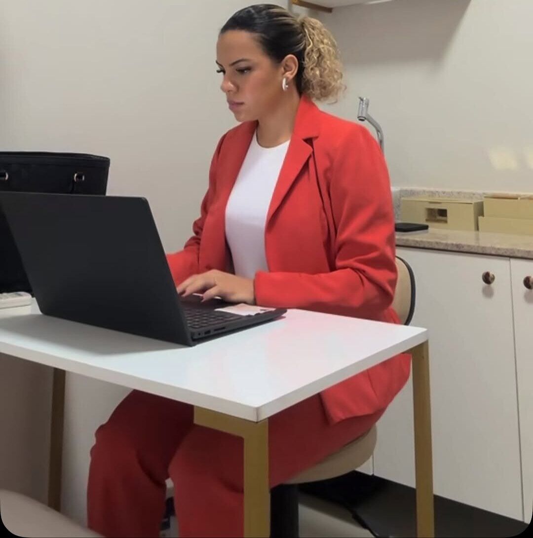 Malu Rilou atendendo no consultório, sentada à mesa com notebook